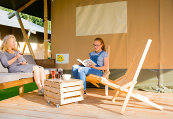 Deux personnes se détendent devant une tente safari au Camping Val d'Or au Luxembourg, boissons à la main.
