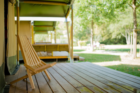 A wooden chair on the porch of a Safari tent at Camping Val d'Or in Luxembourg, surrounded by greenery.