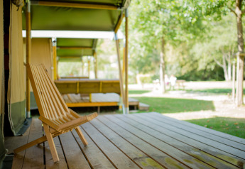 Silla de madera en la terraza de una tienda Safari en Camping Val d'Or, Luxemburgo, rodeada de naturaleza.