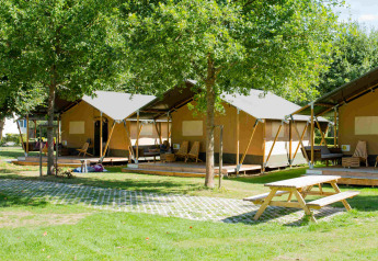 Safari tent lodge at Camping Val d'Or in Luxembourg with green lawns, trees, and picnic benches outside.