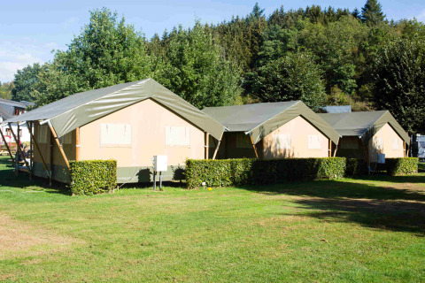 Safari-Zelte auf dem Campingplatz Val d'Or in Luxemburg auf einer grünen Wiese mit Bäumen im Hintergrund.