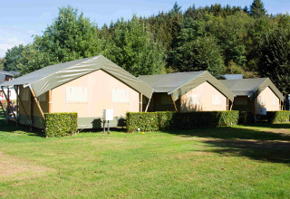 Safari-Zelte auf dem Campingplatz Val d'Or in Luxemburg auf einer grünen Wiese mit Bäumen im Hintergrund.