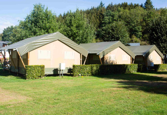 Safaritenten op Camping Val d'Or in Luxemburg, geplaatst op een grasveld met bomen op de achtergrond.