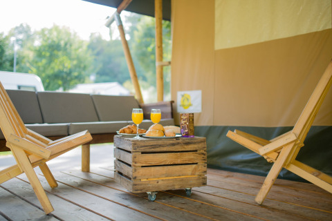 Zona de descanso al aire libre con muebles de madera y desayuno en la tienda Safari, Camping Val d'Or, Luxemburgo.