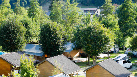 Wooden cabins and tents surrounded by green trees at Camping Val d'Or holiday park in Wiltz, Luxembourg, sunny day.