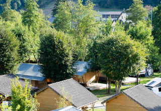 Wooden cabins and tents surrounded by green trees at Camping Val d'Or holiday park in Wiltz, Luxembourg, sunny day.
