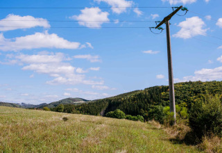 Scenic view of a grassy field, power pole, and lush hills under blue sky at Camping Val d'Or in Wiltz.