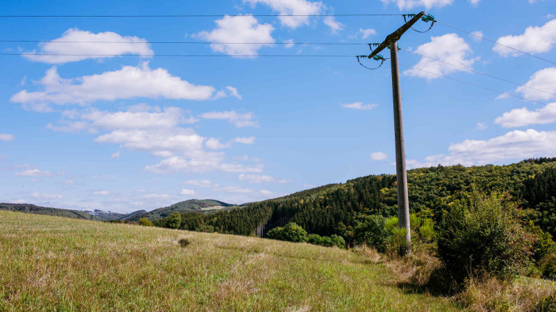 Aussicht auf eine Wiese mit Strommast, sanfte Hügel und blauer Himmel im Camping Val d'Or, Wiltz.