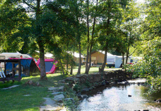 Campingplads ved flod med telte, campingvogne og træer i sollys på Camping Val d'Or i Wiltz, Luxembourg.