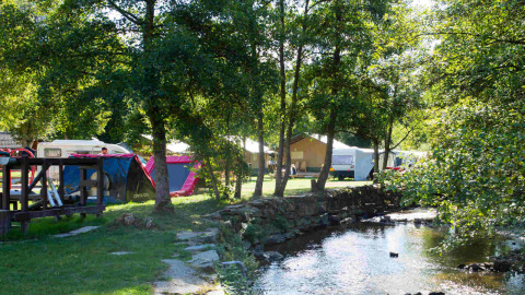 Campsite beside a creek with tents, caravans and trees at Camping Val d'Or in Wiltz, Luxembourg.