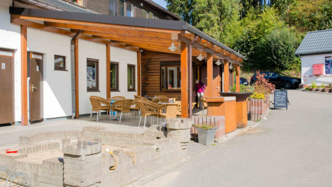 Outdoor terrace with wooden furniture at Camping Val d'Or in Wiltz, Luxembourg, surrounded by greenery.