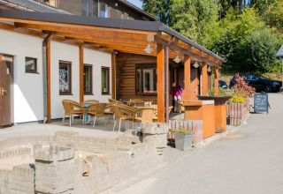 Outdoor terrace with wooden furniture at Camping Val d'Or in Wiltz, Luxembourg, surrounded by greenery.