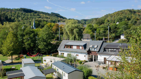 Vista del Camping Val d'Or en Wiltz, Luxemburgo, casas móviles, parque infantil y colinas verdes al fondo.