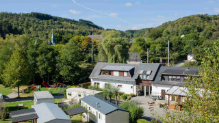 Uitzicht op Camping Val d'Or in Wiltz, Luxemburg, met stacaravans, speeltuin en groene heuvels op de achtergrond.