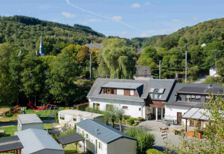 Vista del Camping Val d'Or en Wiltz, Luxemburgo, casas móviles, parque infantil y colinas verdes al fondo.