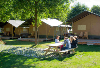 Camping Val d'Or holiday park in Wiltz, Luxembourg, with families sitting at a picnic table by large tents.