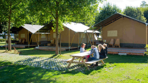 Camping Val d'Or im Ferienpark in Wiltz, Luxemburg, mit Familien am Picknicktisch vor großen Zelten.