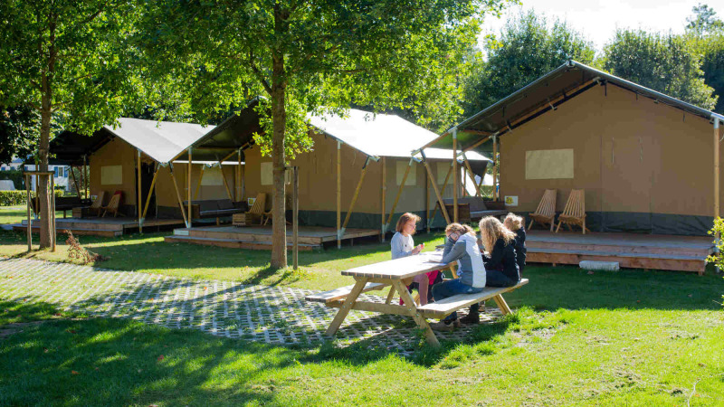 Camping Val d'Or im Ferienpark in Wiltz, Luxemburg, mit Familien am Picknicktisch vor großen Zelten.