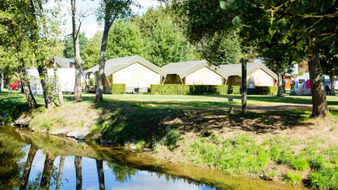 Camping Val d'Or en Wiltz, Luxemburgo, con tiendas de campaña, árboles y un río en un entorno natural tranquilo.