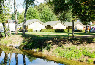 Camping Val d'Or à Wiltz, Luxembourg avec tentes safari, arbres et rivière dans un parc de vacances paisible.