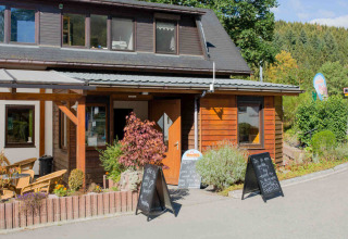 Indgang til Camping Val d'Or feriepark i Wiltz, Luxembourg, med skilte og grønne omgivelser i solskin.
