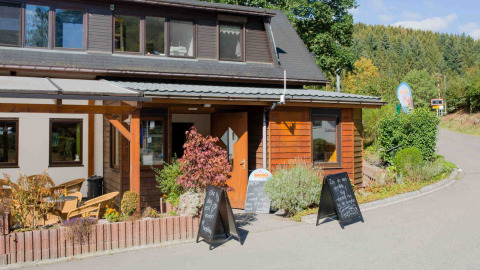 Der Eingang zum Camping Val d'Or Ferienpark in Wiltz, Luxemburg, mit Aufstellern und Pflanzen im Sonnenschein.