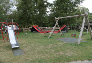 Legeplads med rutsjebane, gynger og klatrestativ på Camping Val d'Or i Wiltz, Luxembourg, omgivet af træer.