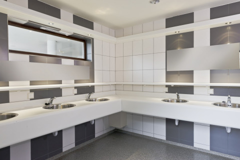 Baño público moderno con varios lavabos, espejos y paredes de azulejos grises y blancos en Wiltz, Luxemburgo.