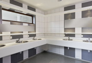 Modern public restroom with multiple sinks, mirrors, and tiled walls in shades of gray and white in Wiltz.