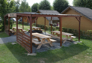 Zona picnic coperta con tavoli di legno presso Camping Val d'Or, villaggio turistico a Wiltz, Lussemburgo.