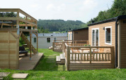 Tiny house lodge op Camping Val d'Or in Luxemburg met houten terras, stoelen en uitzicht op het groen.