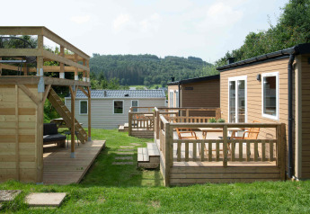 Tiny house lodge på Camping Val d'Or i Luxembourg med træterrasse, stole og udsigt til skovområde.