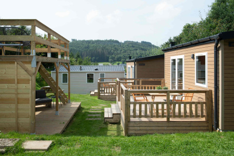 Tiny house lodge bij Camping Val d'Or in Luxemburg met houten terrassen, stoelen en bosrijk uitzicht.
