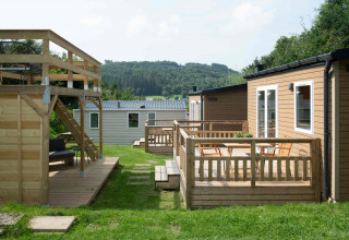 Tiny house al Camping Val d'Or in Lussemburgo con terrazza in legno, sedie all'aperto e vista sul verde.