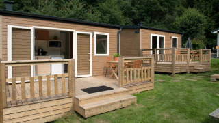 Twee tiny house lodges met houten veranda’s op gras, omringd door bomen in een rustige omgeving.
