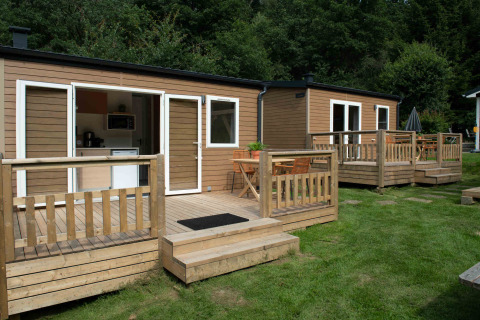 Two tiny house lodges with wooden decks, set on grass and surrounded by trees, peaceful natural setting.