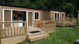 Twee tiny house lodges met houten veranda’s op gras, omringd door bomen in een rustige omgeving.