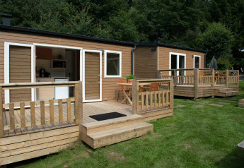 Due tiny house in legno con veranda su prato verde, circondate da alberi e immersi nella natura.