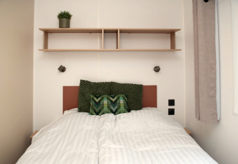 Chambre douillette dans une tiny house à Camping Val d'Or, Luxembourg, avec lit et étagère en bois.