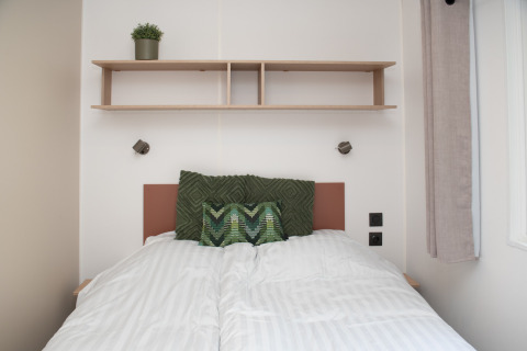 Dormitorio acogedor en tiny house en Camping Val d'Or, Luxemburgo, con cama y estante de madera.