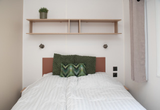 Dormitorio acogedor en tiny house en Camping Val d'Or, Luxemburgo, con cama y estante de madera.