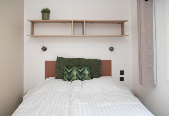 Chambre douillette dans une tiny house à Camping Val d'Or, Luxembourg, avec lit et étagère en bois.