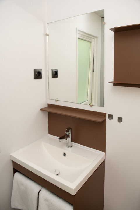 Bagno moderno con lavandino bianco, specchio e mensole marroni nel Tiny house al Camping Val d'Or, Lussemburgo.