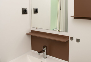 Baño moderno con lavabo blanco, espejo y estantes marrones en Tiny house de Camping Val d'Or, Luxemburgo.