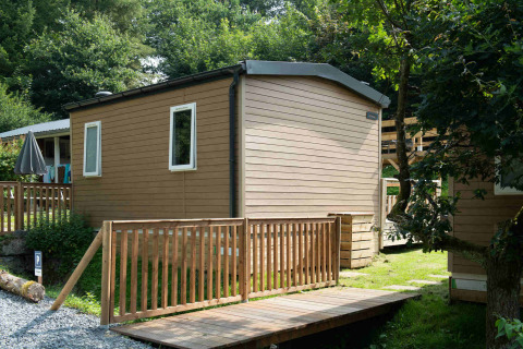 Tiny house lodge at Camping Val d'Or in Luxembourg, featuring wooden walls and a deck surrounded by trees.