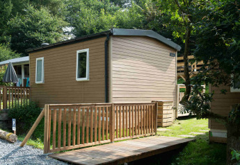Tiny house lodge at Camping Val d'Or in Luxembourg, featuring wooden walls and a deck surrounded by trees.