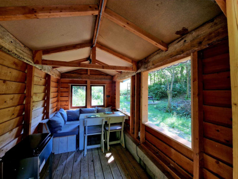 Interior de la Boslodge um Bierg en Camping Val d'Or, Luxemburgo, con sofá, mesa y vista al bosque.