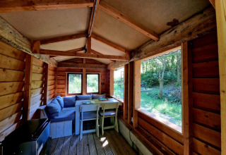 Interior de la Boslodge um Bierg en Camping Val d'Or, Luxemburgo, con sofá, mesa y vista al bosque.