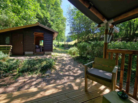 Udsigt fra verandaen ved Boslodge um Bierg, med træhytte og omgivet af grønne træer om sommeren.
