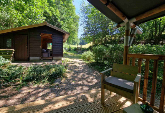 Zicht vanaf het terras bij Boslodge um Bierg, met een houten hutje omgeven door groene natuur.